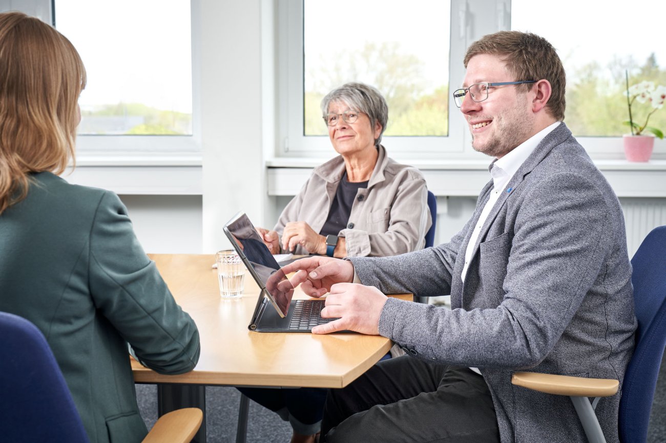 Drei Personen sitzen in einem hellen Büro an einem Besprechungstisch
