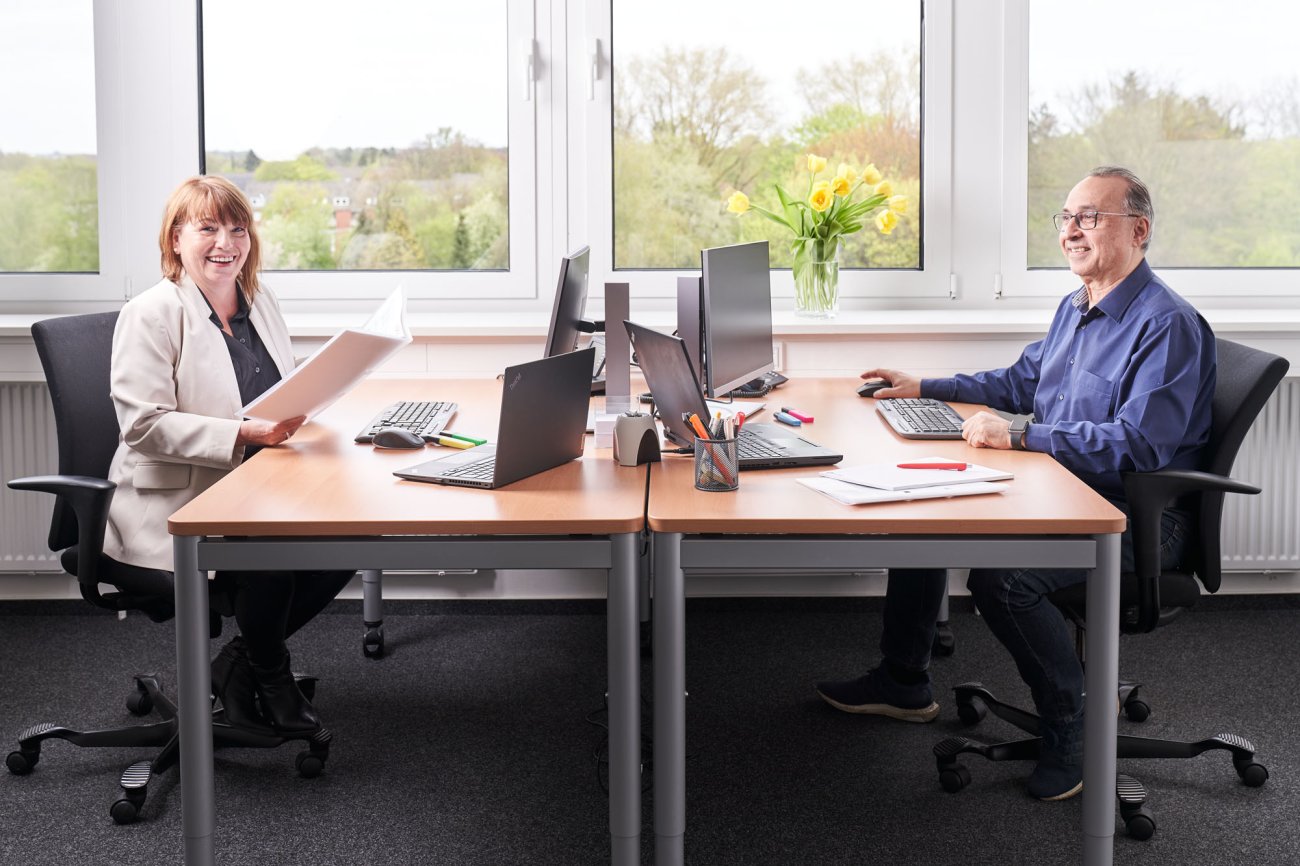 Zwei Mitarbeiter arbeiten an einem Doppel-Schreibtisch in einem hellen Büro
